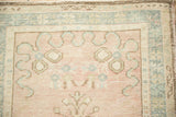 Vintage distressed Oushak rug corner showing dusty rose field and pale blue cloudband motif.