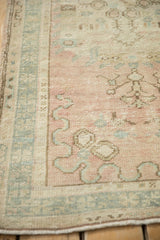 Distressed vintage Oushak rug detail with dusty rose field, muted green border, and stylized curvilinear motifs.