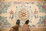 Distressed vintage Oushak rug runner with starburst medallion and blush floral bouquets on ivory, underfoot.