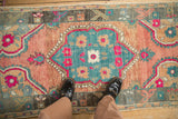 A person's view of a distressed vintage Oushak rug, highlighting the colorful teal and melon floral medallion.