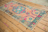 Angled view of a distressed Oushak rug with vibrant teal and fuchsia florals on a cantaloupe field.