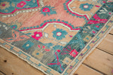 A corner view of the distressed Oushak rug's charcoal spandrel and teal border with fuchsia accents.
