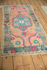 Angled view of a distressed Oushak rug with a vibrant teal, fuchsia, and cantaloupe melon design.