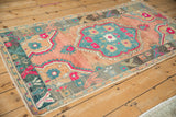 Angled view of a distressed Oushak rug highlighting its cantaloupe, teal, and fuchsia floral design.