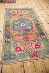 Angled view of a distressed vintage Oushak rug with a vibrant teal and fuchsia floral medallion.