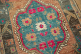 Close-up on the low-pile texture of a distressed Oushak rug with fuchsia and teal floral motifs.