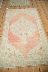 Angled view of the vintage Oushak rug highlighting its oversized medallion on a dusty melon field.