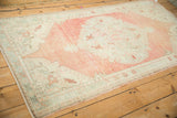Low angle view of a distressed Oushak rug with time-softened melon and seafoam colors.