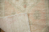 Corner of a distressed Oushak rug folded to show the hand knotted foundation and side selvage.