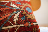 Close-up of hand-knotted rug pillow pile with geometric patterns in red, blue, and cream.