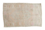Vintage distressed Oushak rug with an elongated hexagonal medallion in pale beige, slate blue, and pink.