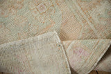 Folded corner of a distressed vintage Oushak rug reveals its low pile texture and hand-woven foundation.