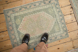 Pale pink medallion, hook relief, and olive green pattern on distressed Oushak rug.