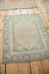 Distressed Oushak rug corner revealing pale pink and olive green tones with side cord.