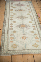Distressed Oushak runner with ivory, gold, and pale brown geometric motifs and patterned border.