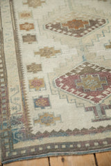 Corner of distressed Oushak runner, showing muted ivory, gold, raspberry red geometric motifs and border.