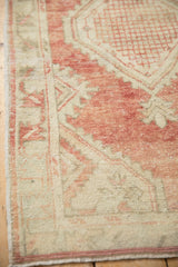 Distressed Oushak rug corner with dusty red, ivory serrated border, and short fringe.