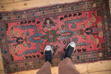 Vintage Mehreban rug runner with feet from above, displaying its geometric palmettes and visible surface wear.