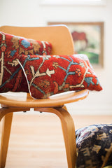 Close-up of a vintage Persian rug pillow with deep red field, blue, cream patterns, white piping.