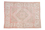 A vintage distressed Oushak carpet with a geometric diamond medallion in dusty blush, ivory, and pale beige tones.