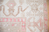Close-up of the distressed Oushak carpet's low pile showing the geometric cloudband design in dusty blush and beige.