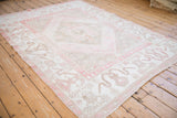 Soft blush pink and ivory tones on a distressed Turkish Oushak carpet viewed at an angle.