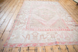 Angled perspective of a distressed vintage Oushak carpet with a faded blush, ivory, and beige pattern.