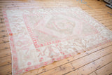 Distressed vintage Oushak carpet seen from an angle, showing the faded geometric pattern in blush pink and beige.
