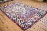 Distressed vintage Oushak rug with worn violet, ivory, and rust geometric patterns.
