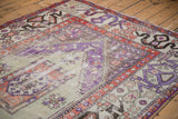 Distressed violet, ivory, and rust Oushak carpet section with geometric border and visible knot wear.