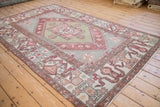 Angled view of a vintage Oushak carpet with a geometric medallion, cloudband border, and distressed patina.