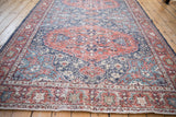 Distressed Turkish Sparta rug corner, terra cotta and navy floral patterns, visible wear.