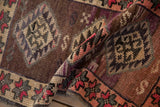 Folded vintage Kars rug mat shows distressed abrash pile, geometric border in plum, pink, and ivory.