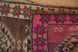 Distressed Kars rug detail: abrash-rich pink, aubergine geometric patterns, visible knot heads, rustic fringe.
