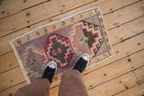 A distressed vintage Kars rug mat shown to scale with mauve and brown geometric medallions.