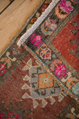 Distressed Kars rug mat corner, with white fringe and vibrant border of pink, purple, orange motifs.