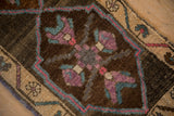 Primitive quatrefoil floral motif in dusty mauve and slate blue on abrashed brown ground.