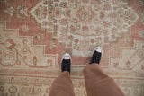 Distressed Oushak rug with abrashed dusty rose field and faded floral motifs.