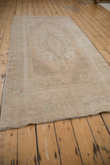 Full length view of a distressed Oushak runner showing its slightly bowed side and soft, even wear.