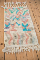 Angled view of a Moroccan rug mat showing its plush ivory pile and colorful abstract geometric patterns.