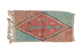 Small Moroccan rug mat with a geometric diamond medallion in faded ruby red and pale turquoise blue.
