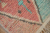 Evenly piled corner of a Moroccan rug showing soft red, turquoise, and charcoal geometric details.