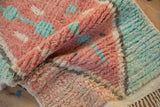 A folded corner of a Moroccan rug highlighting its plush hand-knotted texture in soft pink and turquoise.