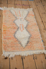 Corner of a Moroccan rug with a shaggy pile and knotted cream fringe.