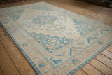 Angled view of the distressed vintage Oushak carpet, showing its stepped medallion and soft beige and blue tones.