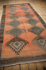 Distressed texture of serrated diamond motifs and geometric border in terracotta and silver tones.