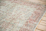 Corner of a distressed Sparta carpet showing worn texture, scrolling vines, and thousand flower border.