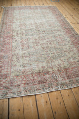 Angled view of a distressed Sparta carpet's soft patina, with dusty red scrolling vines and a floral border.