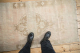 Distressed Oushak rug featuring heavy abrashes across faded dusty rose and ivory tones.