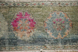 Magenta floral motif on distressed Oushak pile, showing moss green abrash and worn foundation.